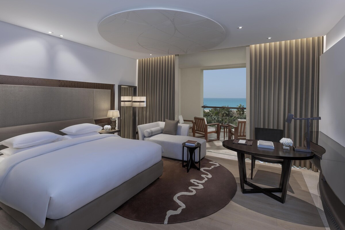 Une chambre d’hôtel moderne avec un grand lit, un canapé, une petite table et une vue sur l’océan.