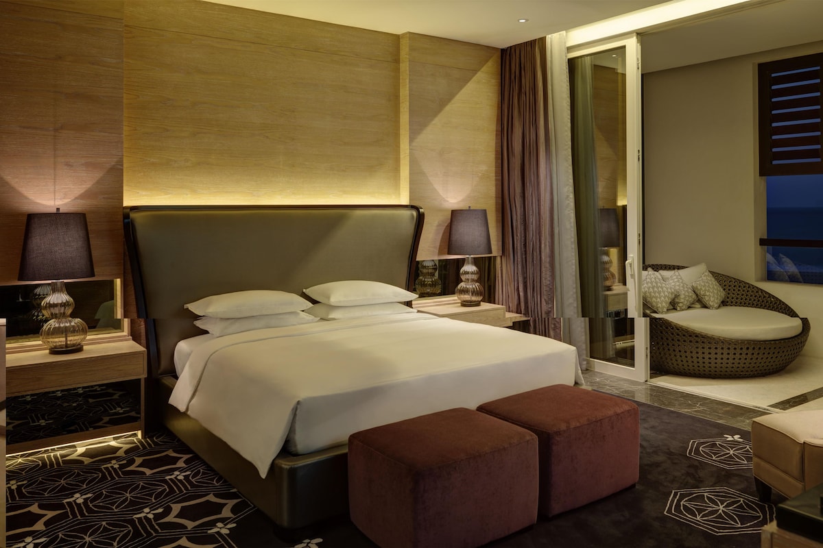 A modern hotel room with a large bed, a seating area, and a view of the night sky.