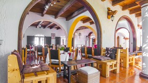 Un amplio comedor con mesas y sillas de madera, techos altos con vigas a la vista y grandes puertas arqueadas.