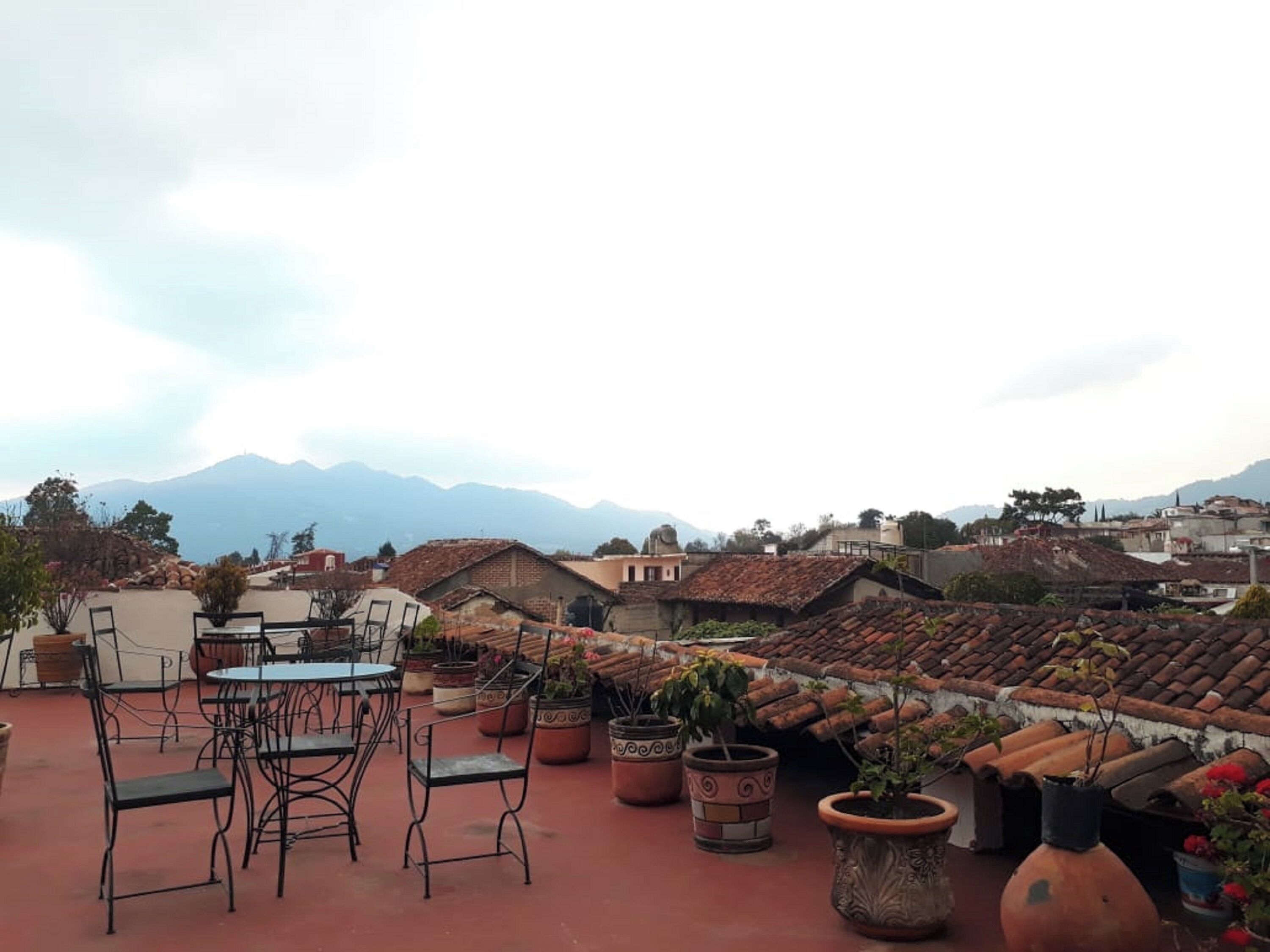 Una terraza en la azotea con mobiliario exterior, plantas en macetas y vistas a un paisaje montañoso.