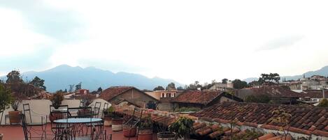 Una terraza en la azotea con mobiliario exterior, plantas en macetas y vistas a un paisaje montañoso.