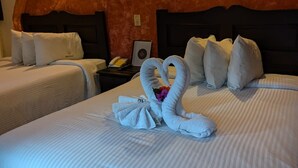 Habitación de hotel con dos camas, cada una con ropa de cama y almohadas blancas. Hay una pared grande, curva y de color marrón rojizo sobre las camas, y una pequeña mesa con una lámpara y un teléfono.