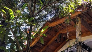 Un hotel con balcón de madera, abundante vegetación y baranda de hierro forjado.
