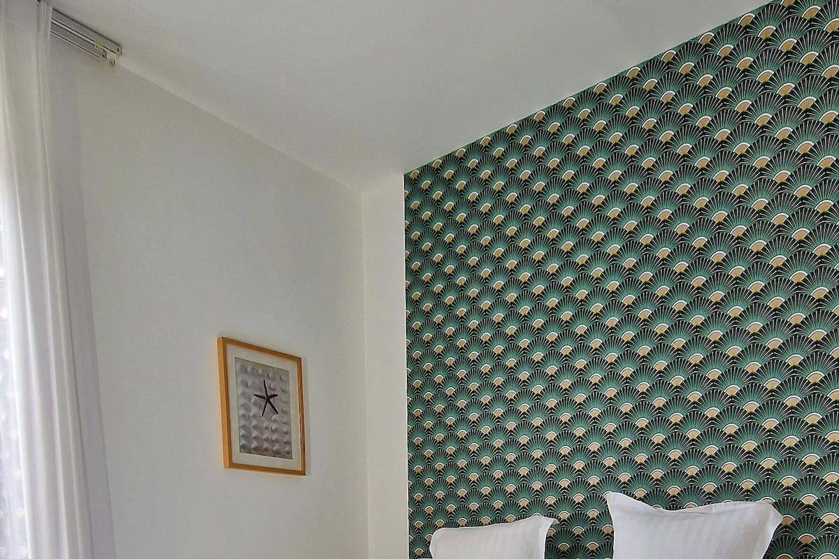 A hotel room with a large bed, a red carpet, a green patterned wall, and a clock on the wall.