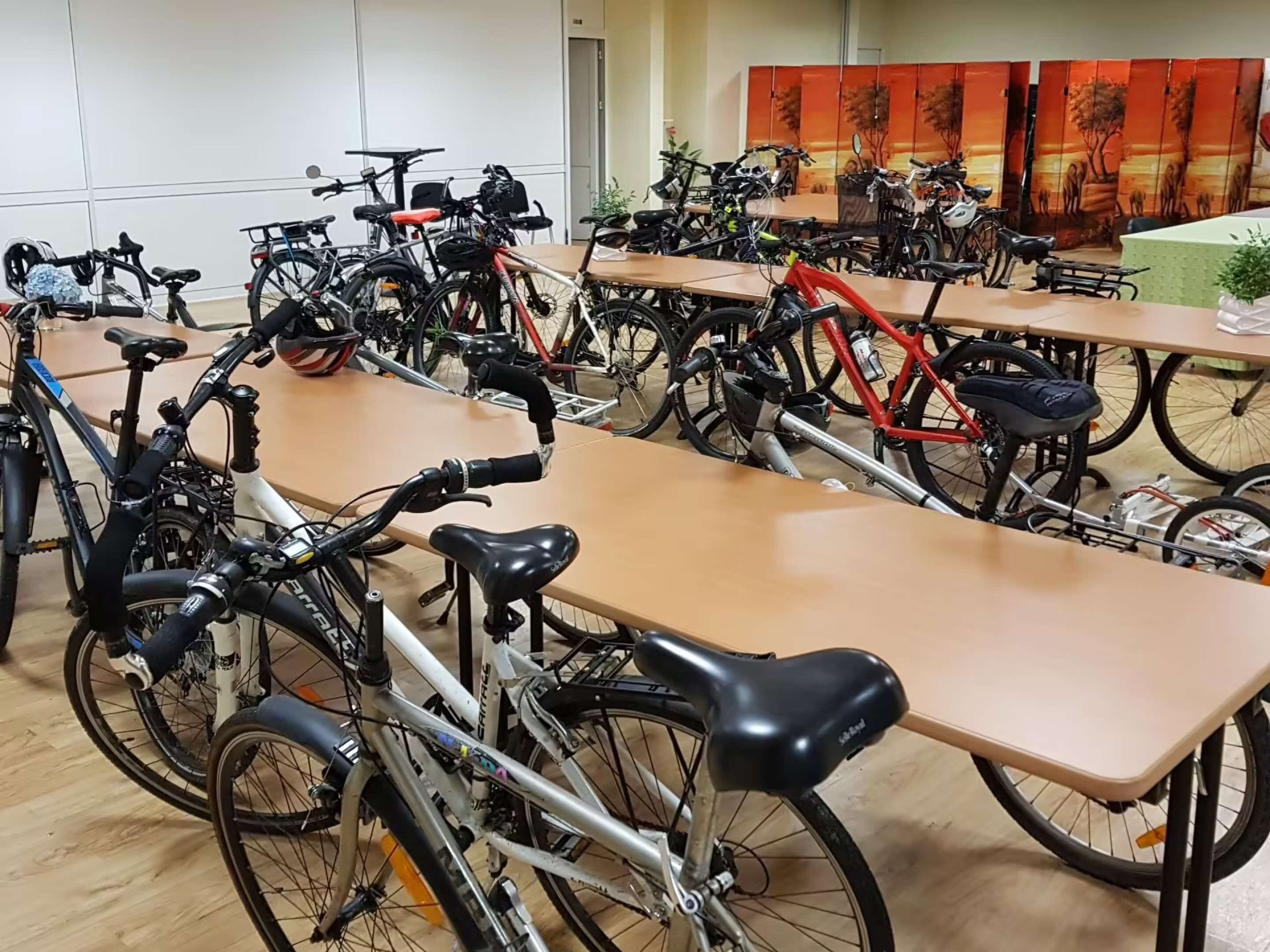 Habitación con varias bicicletas estacionadas junto a mesas, una puerta y una pared con un panel decorativo.