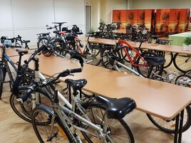 Habitación con varias bicicletas estacionadas junto a mesas, una puerta y una pared con un panel decorativo.