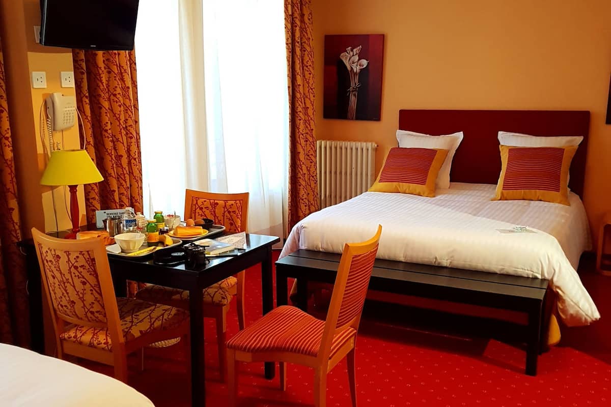 A hotel room with a bed, a desk with a lamp, a chair, and a telephone.