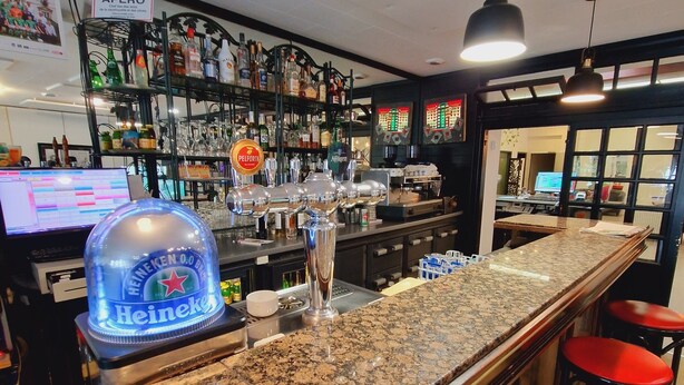A bar area with a granite countertop, bar stools, and a Heineken branded cooler.