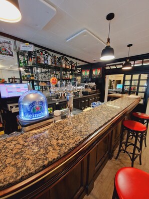 A bar area with a granite countertop, bar stools, and a Heineken branded cooler.