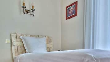 A hotel room with a bed, a red carpet, a white headboard, a wall-mounted light fixture, and a framed picture.
