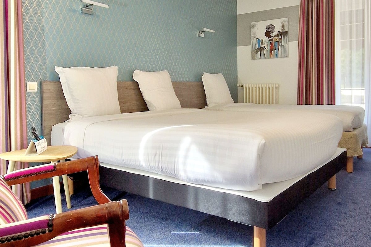 A hotel room with a large bed, a bedside table, a chair, and a window with curtains.