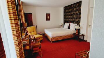 Een hotelkamer met een bed, een stoel, een bureau, een lamp en een roodgekleurd tapijt.