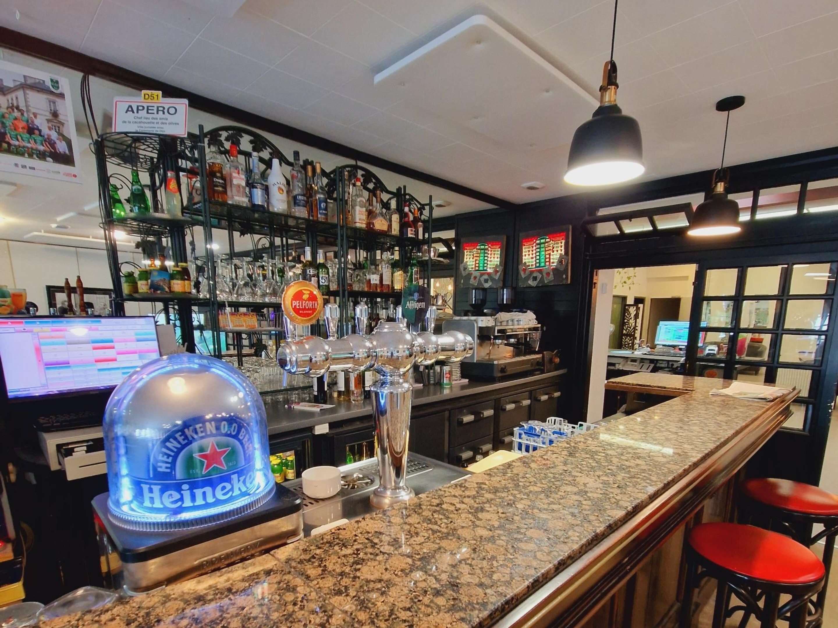 Een bar met een granieten aanrecht, barstoelen, een Heineken-koeler en diverse flessen drank op planken.