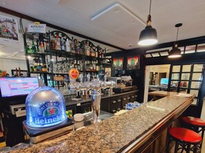 A bar area with a granite countertop, bar stools, a Heineken cooler, and a variety of liquor bottles on shelves.