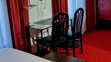 A hotel room with a bed, a table with chairs, a TV, and red curtains.