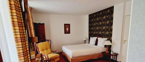A hotel room with a bed, a chair, a desk, a red carpet, and a patterned wall.