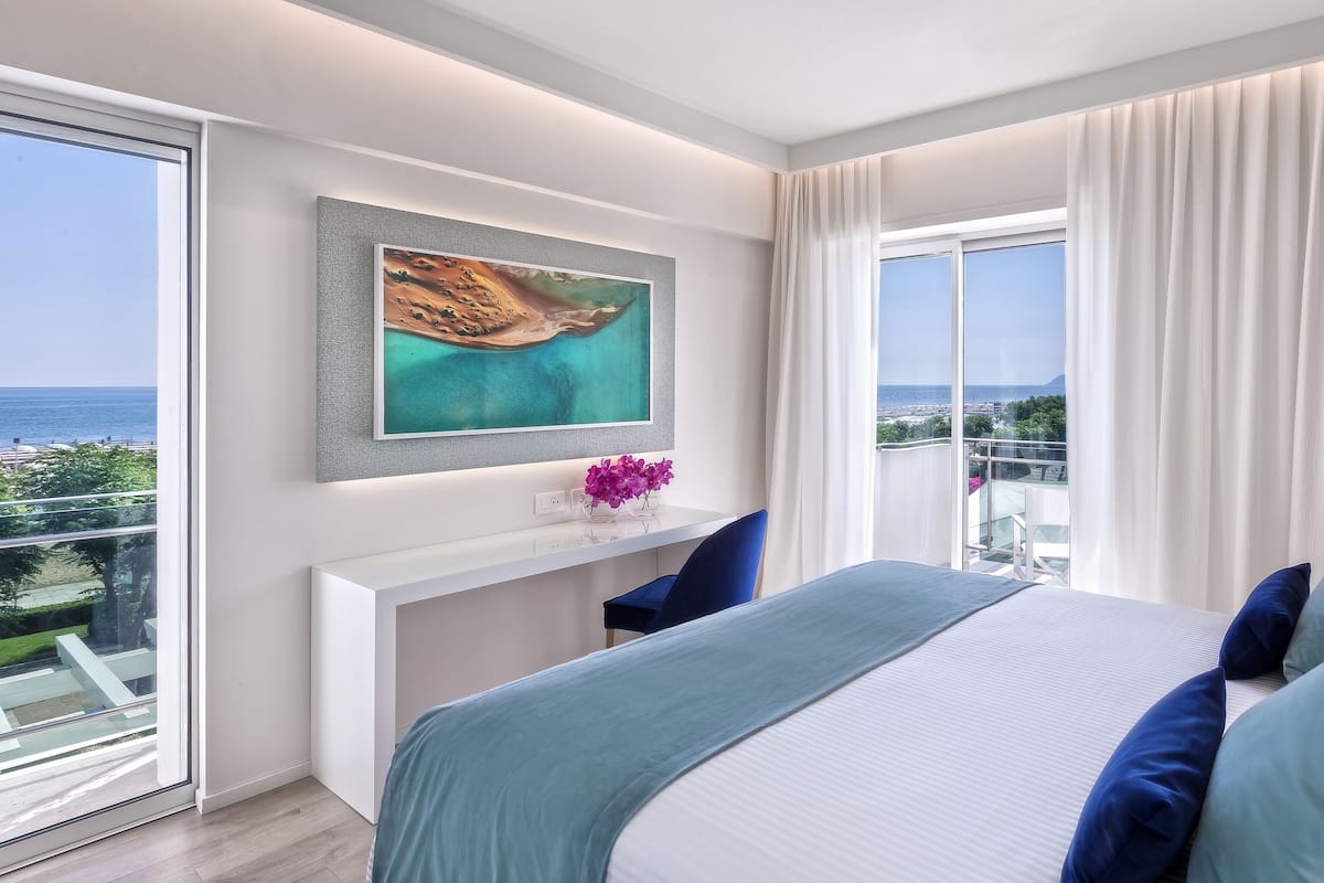 A modern bedroom with a large bed, a desk, and a view of the ocean.