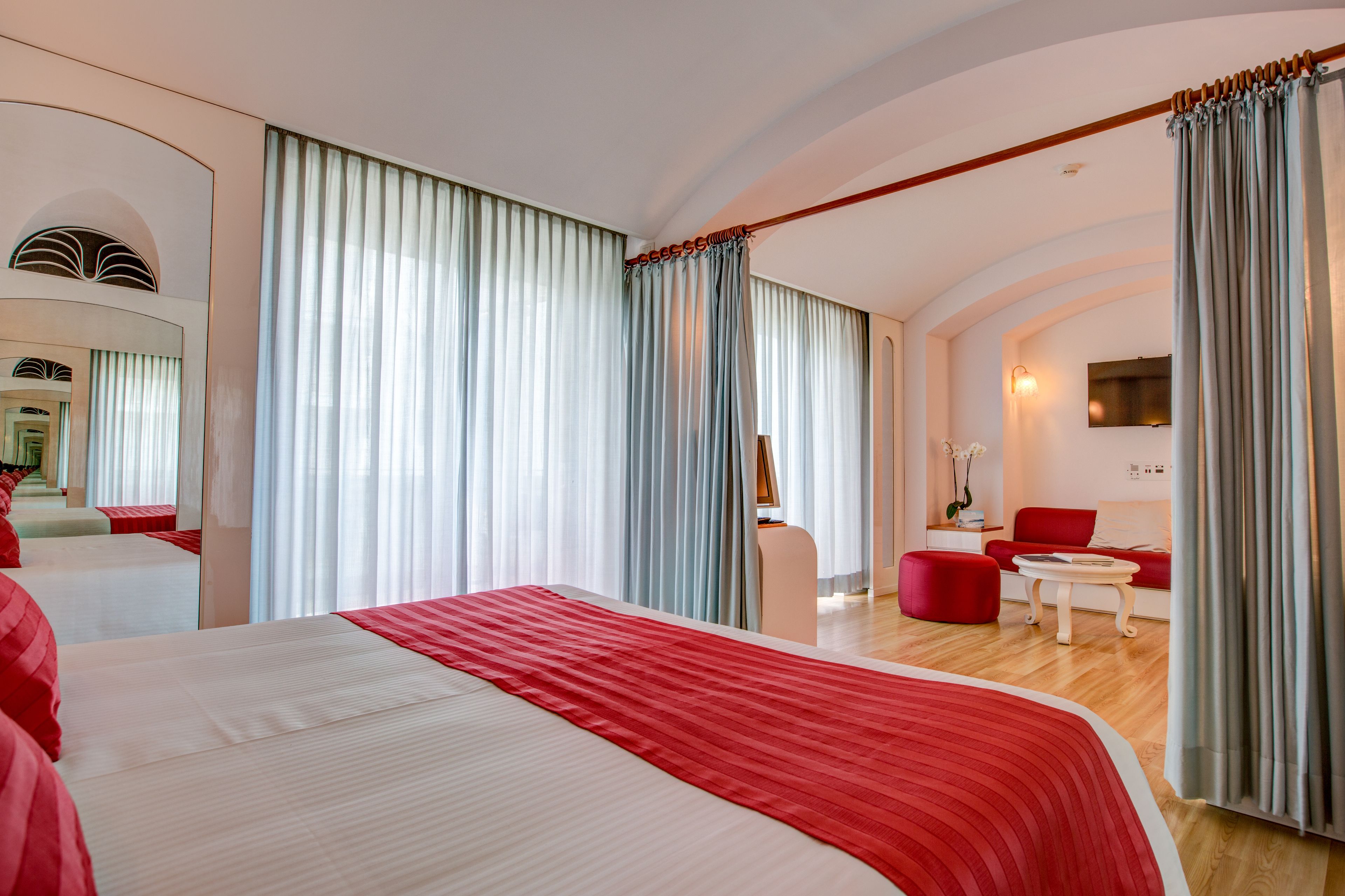 A hotel room with a large bed, a sitting area with a red sofa, and a dining table.