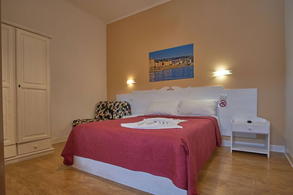 A bedroom with a bed, a nightstand, a pillow, a blanket, and a wall-mounted picture.