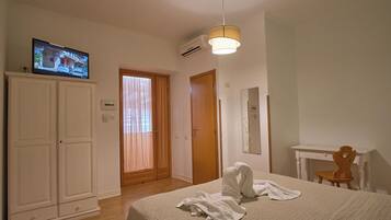 Un dormitorio con una cama, un televisor sobre un mueble, una puerta de madera y un escritorio con una silla.