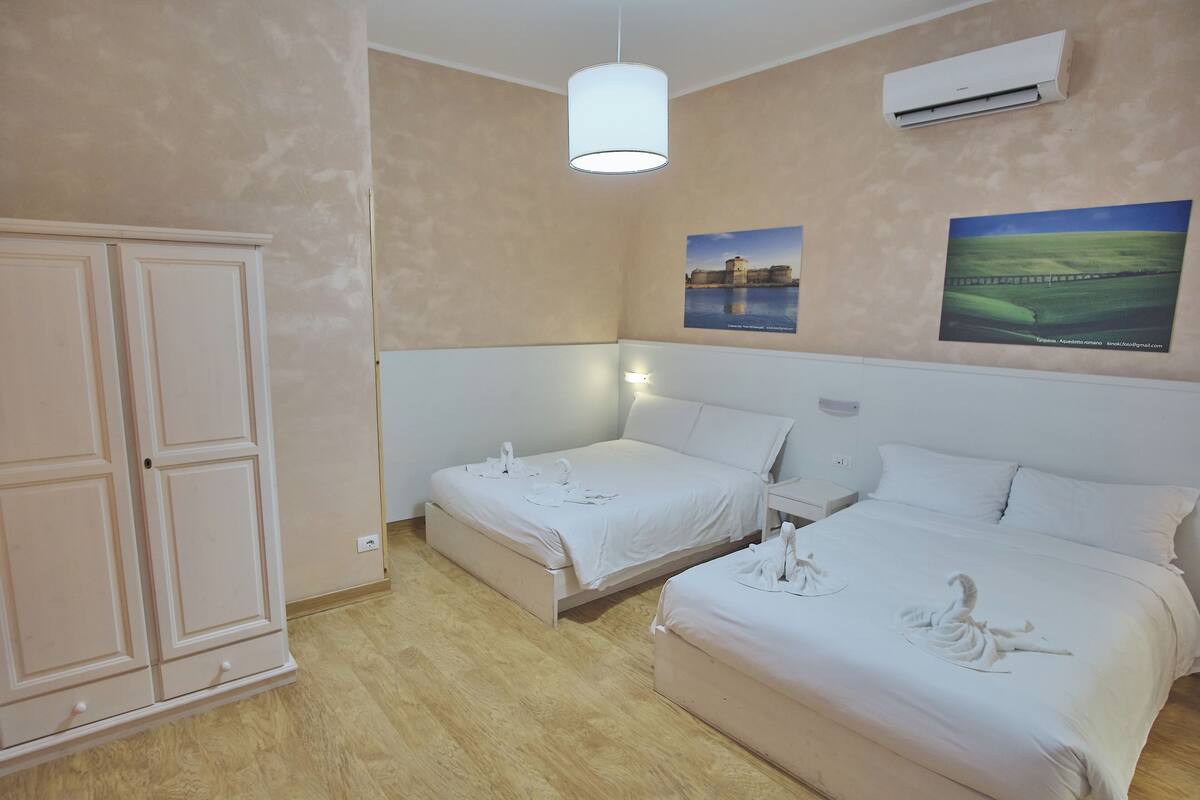A hotel room with two beds, a wardrobe, a hanging light fixture, and two wall-mounted air conditioners.
