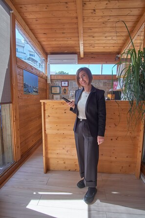 A person standing in a wooden room with a wooden desk, a window, and a plant. - Bel Sole (Civitavecchia)