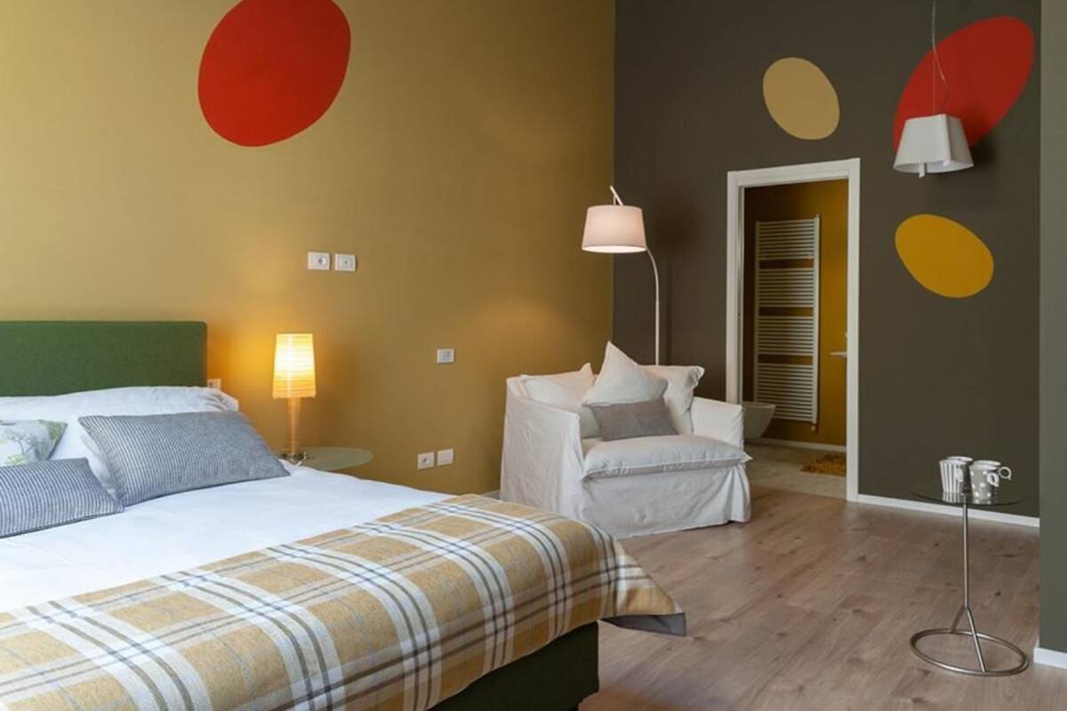 A hotel room with a bed, a chair, a lamp, and a table.