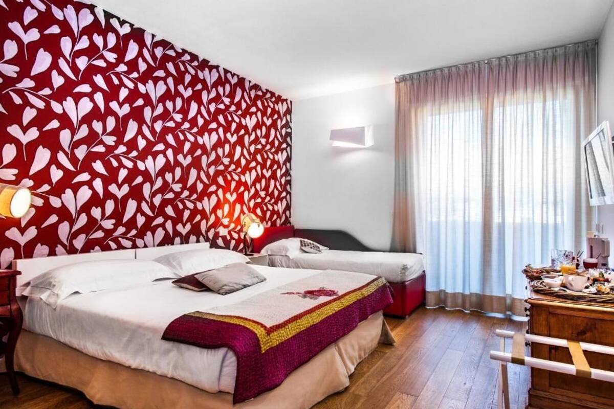 A hotel room with a large bed, a smaller bed, a wooden dresser, and a red patterned wall.