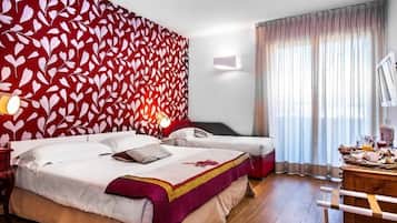 Habitació d'hotel amb un llit gran, un altre més petit, un taulell de fusta i una paret amb un dibuix vermell.
