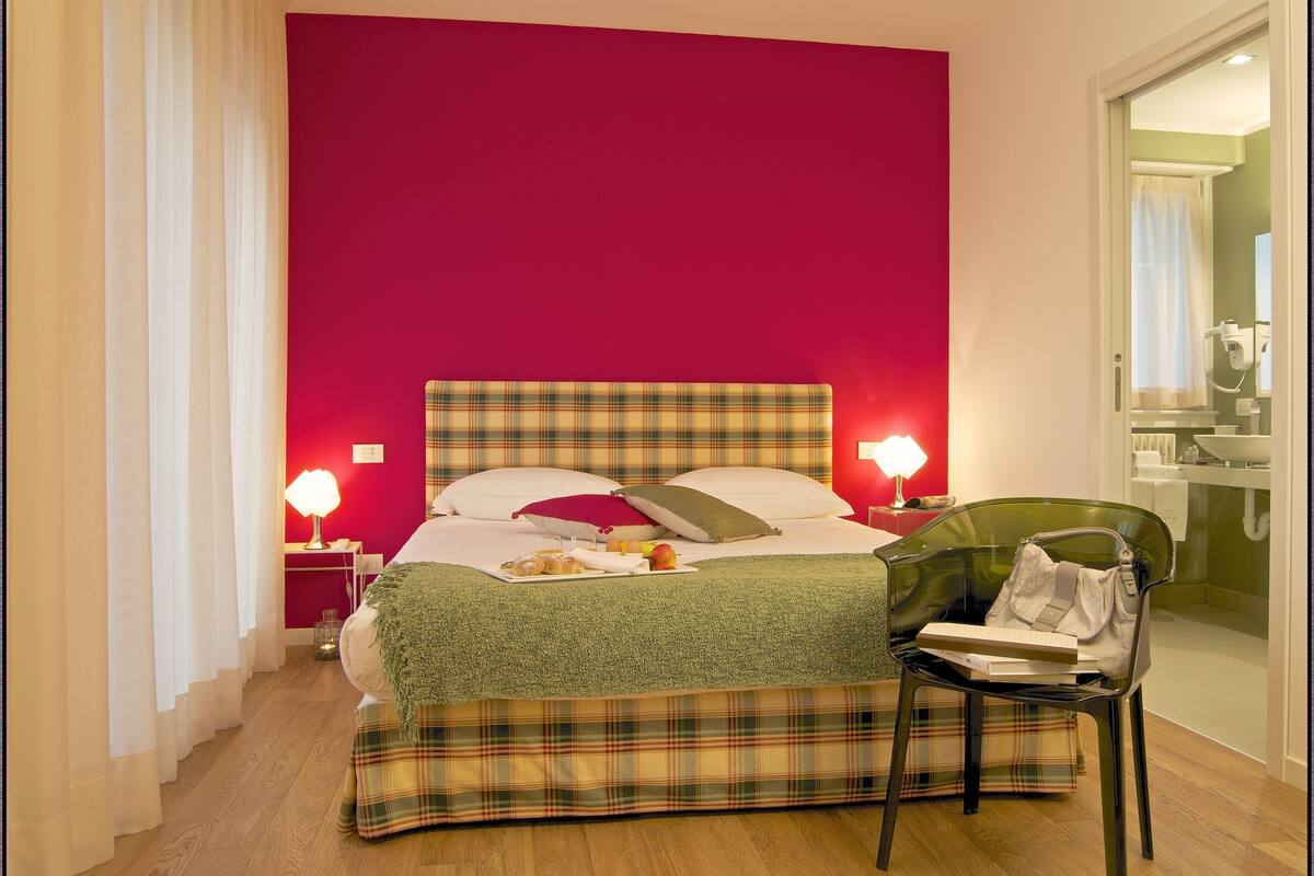 A hotel room with a bed, a chair, a nightstand, and a bathroom visible through an open door.