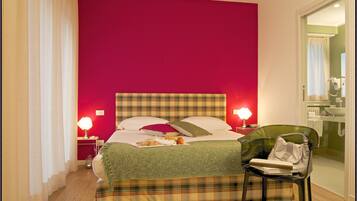 Une chambre d’hôtel avec un lit, une chaise, une table de chevet et une salle de bain visible à travers une porte ouverte.