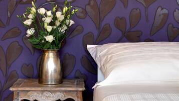 Un dormitorio con una cama, una mesita de noche con un florero y una pared decorada con hojas moradas.