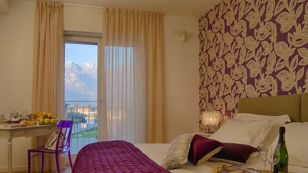 Habitación de hotel con una cama, un escritorio con cosas para el desayuno, una silla y vistas a las montañas por la ventana.