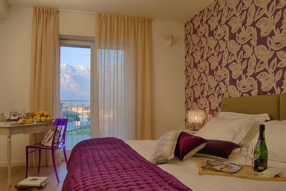 A hotel room with a bed, a desk with breakfast items, a chair, and a view of mountains through the window.