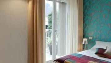 A bedroom with a large bed, a sliding glass door to a balcony, and a teal patterned wall.
