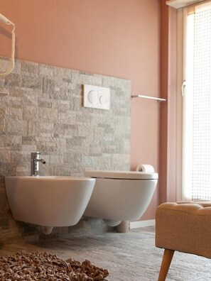 A bathroom with a stone wall, a bidet, a toilet, and a towel rack. - Spluga Sosta & Hotel (Dubino)
