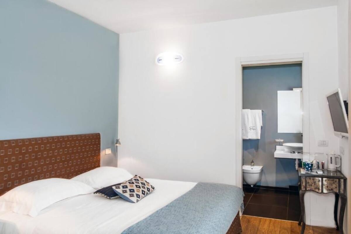 A hotel room with a bed, a small desk with a computer, a sink, and a mirror.