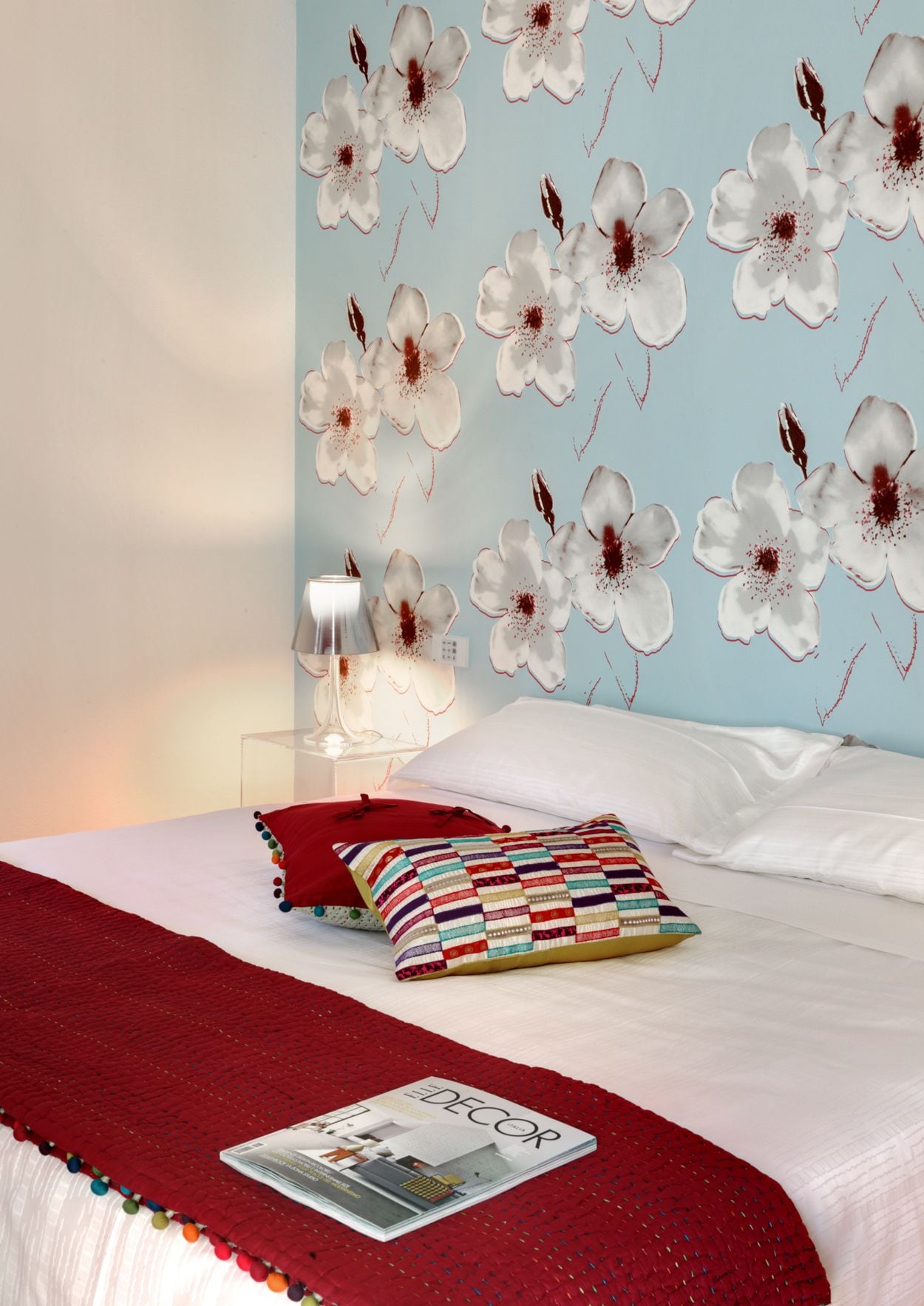 A bedroom with a bed, a red blanket, and a magazine on the bed.