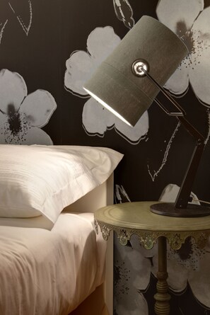 A bed with white bedding, a lamp on a small table, and a wall with a floral pattern. - Spluga Sosta & Hotel (Dubino)