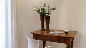 Un escritorio de madera con dos jarrones de mimbre que contienen flores blancas, una silla blanca y una mesita con una taza y un libro.