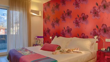 Habitación de hotel con una cama grande, una ventana con cortinas, una pared con estampado floral y una mesita de noche con lámpara.