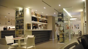 Un área de bar moderna con sillas blancas, estantes llenos de botellas y una vitrina de vidrio.
