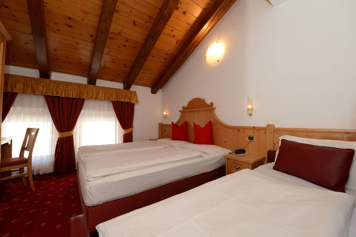 A hotel room with two beds, wooden headboards, and a red carpet.
