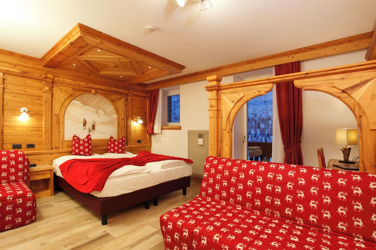 A wooden room with a bed, a sofa, and a window with curtains.