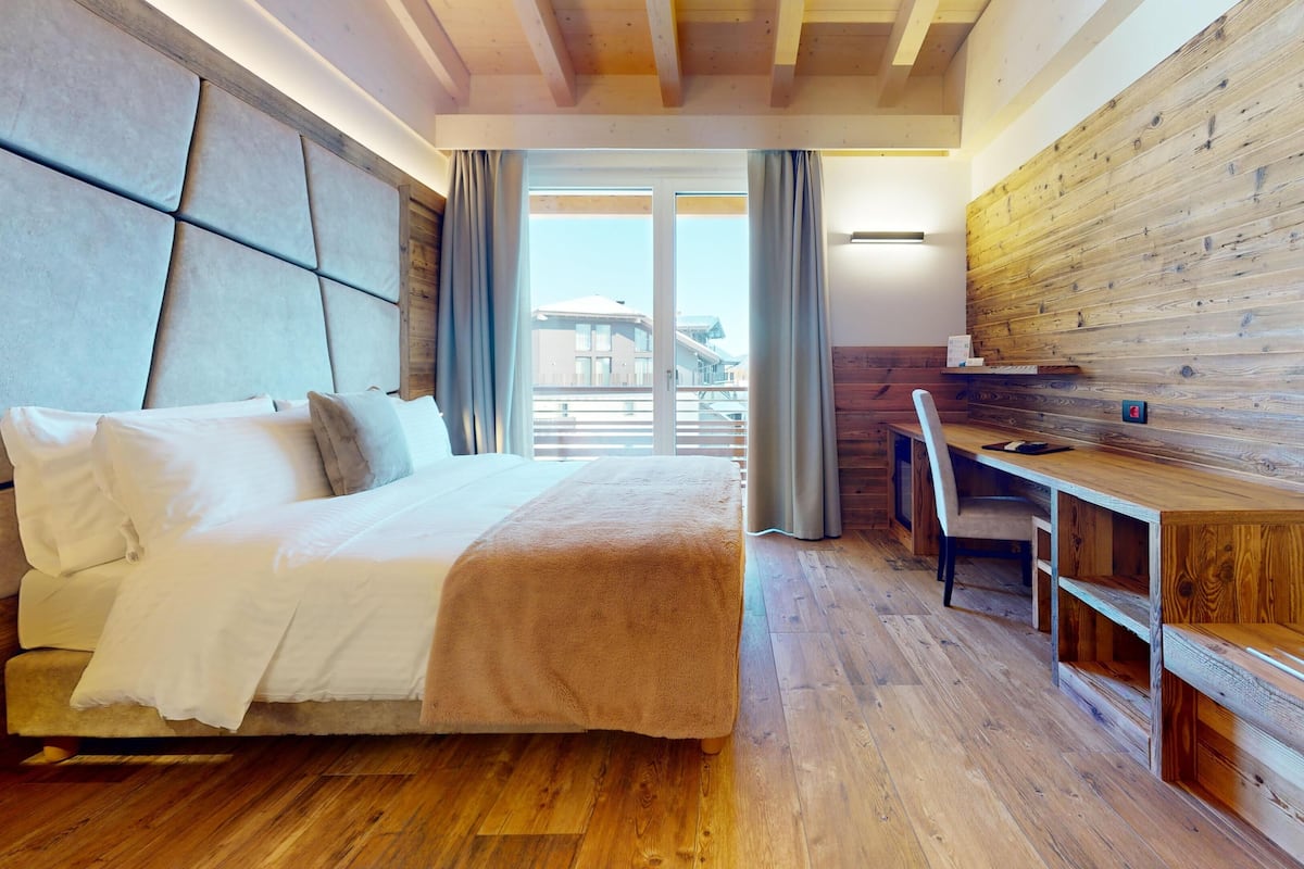 A modern hotel room with a large bed, a wooden desk, and a view of the city.
