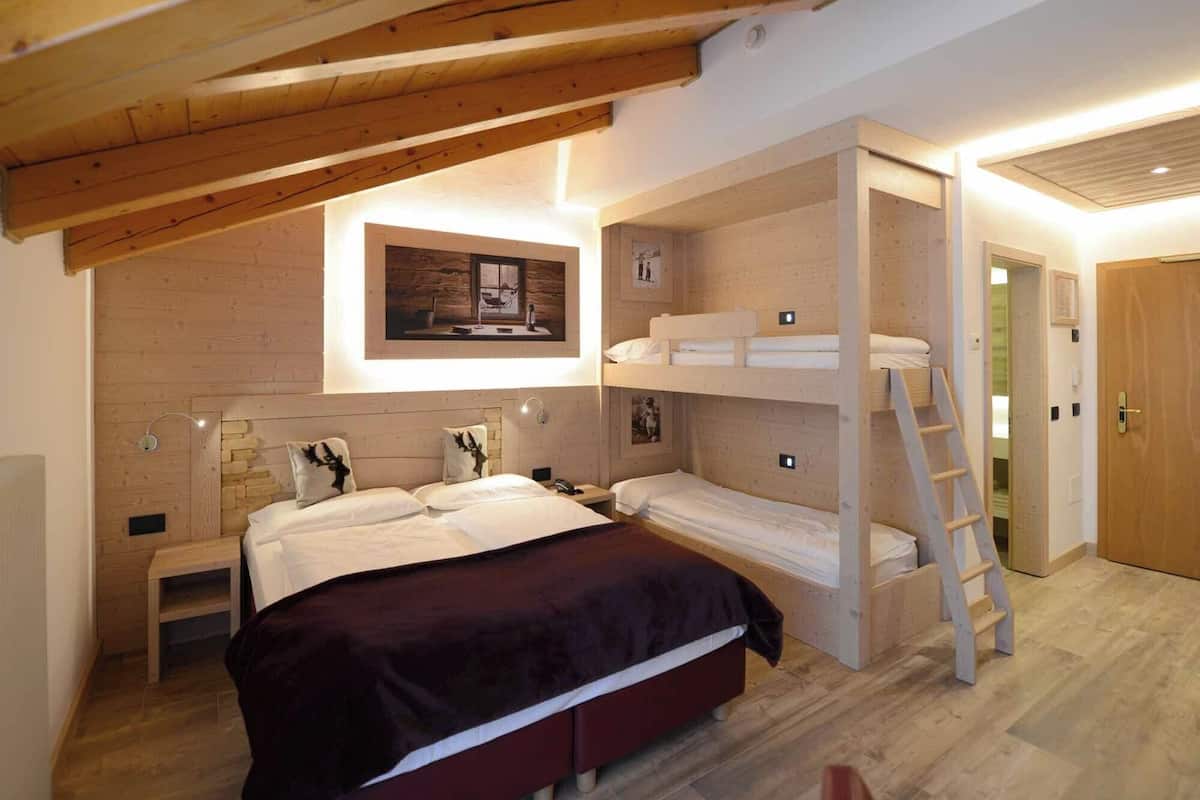 A bedroom with a bunk bed, a single bed, a wooden ladder, and a framed picture on the wall.