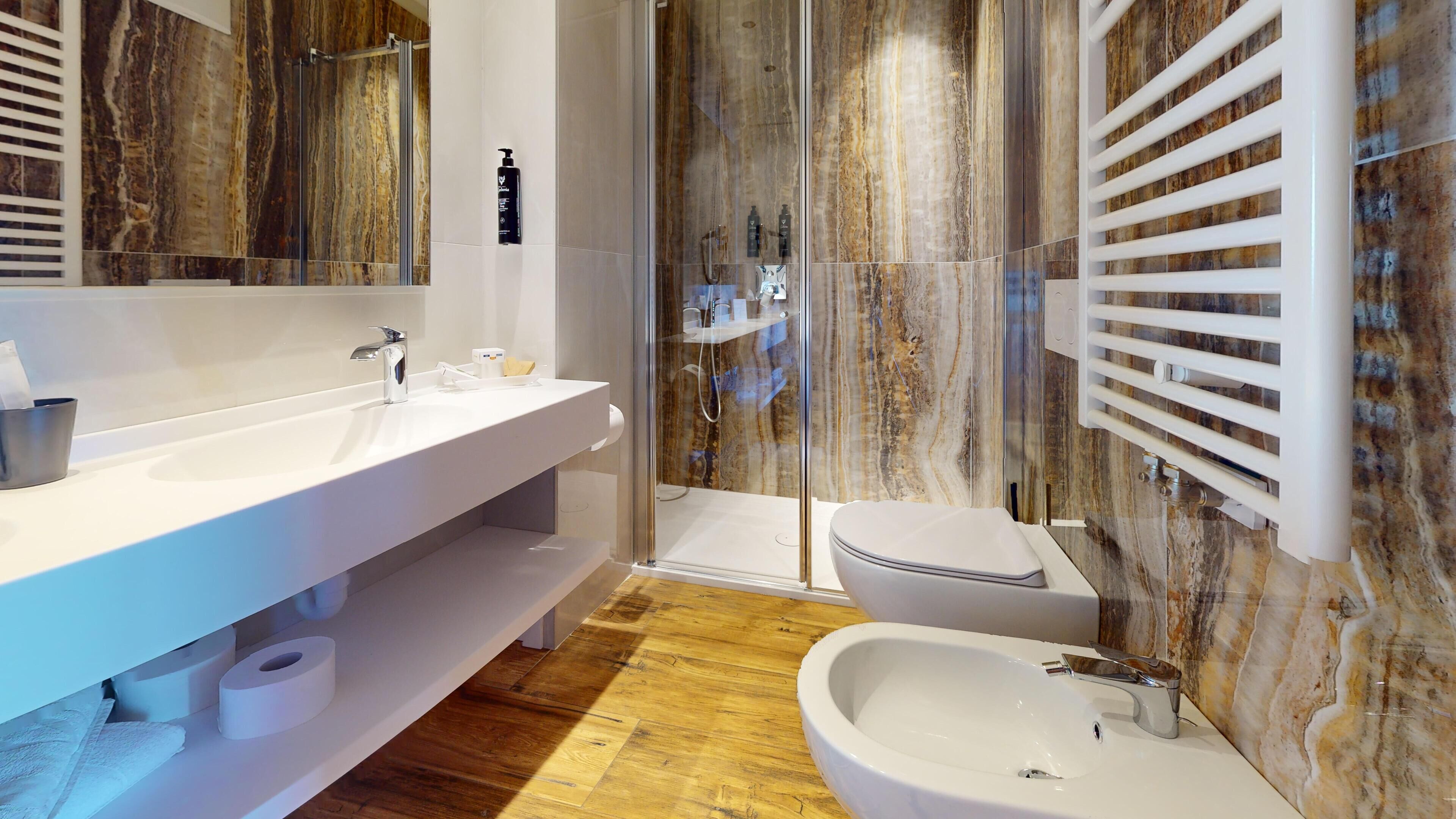 A modern bathroom with a large mirror, a white sink, a shower enclosure, and a bidet.