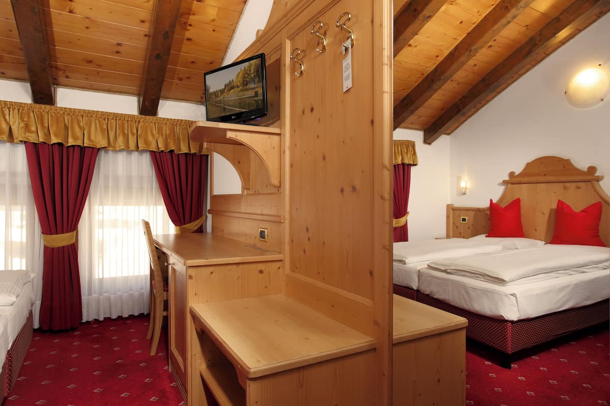 A wooden room with a bed, a desk, and a television on a shelf.