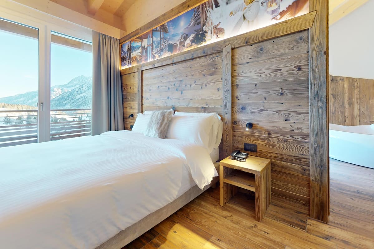 A bedroom with a large bed, wooden headboard, and a view of mountains through a large window.