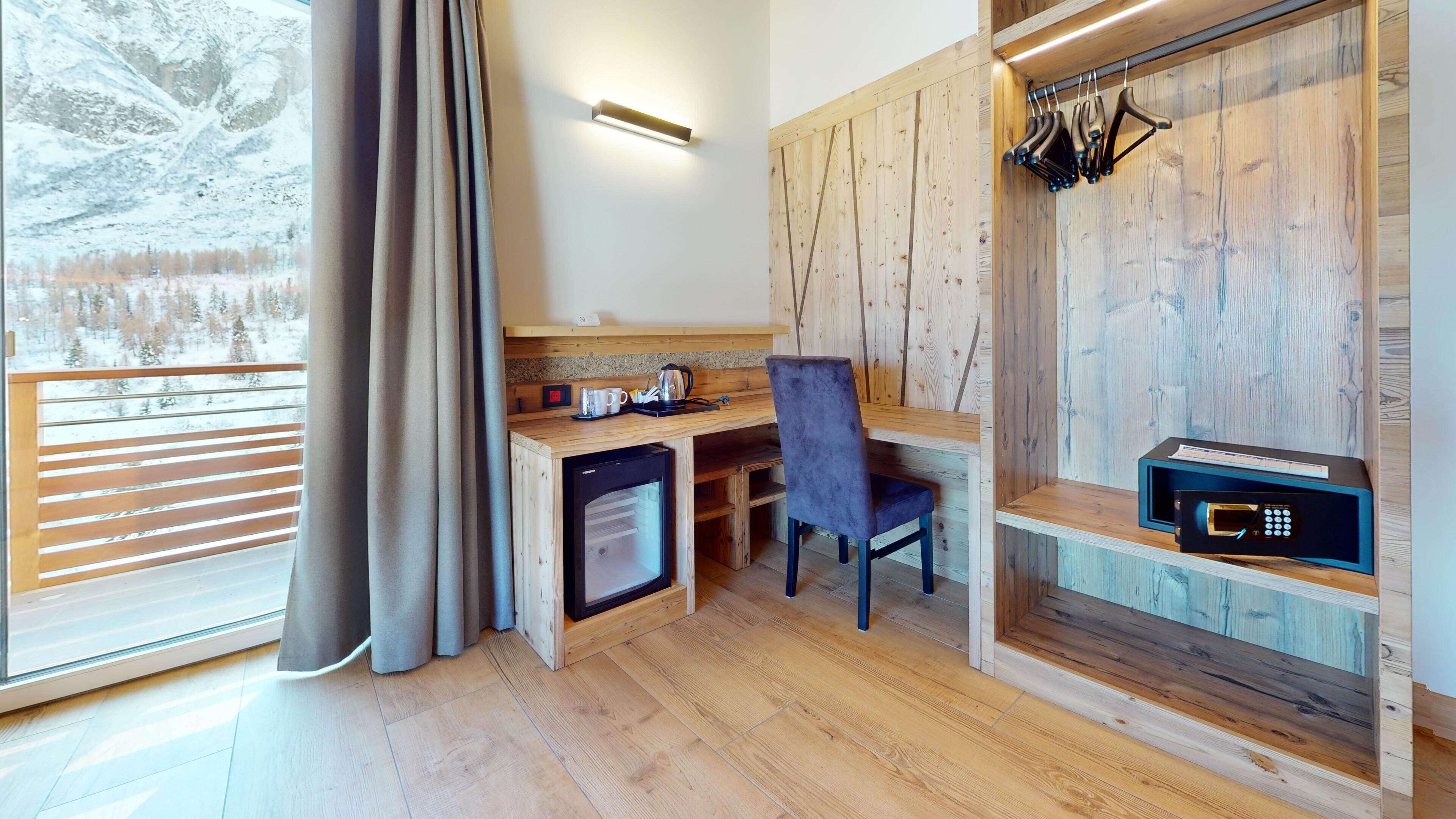 A cozy room with a wooden desk, chair, and a small kitchenette area.